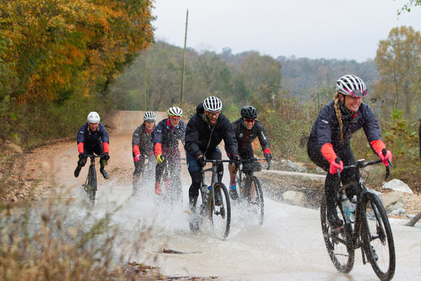 Bikers ride down a wet dirt path 