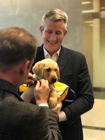 PenFed Credit Union CEO and President and PenFed Foundation CEO James Schenck ties service dog in-training vest on WestPoint, the newest member of the PenFed team from Canine Companions for Independence, as he prepares for his first day of duty at PenFed headquarters.