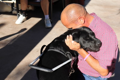 A visually impaired guide dog user, hugging his black lab guide dog.