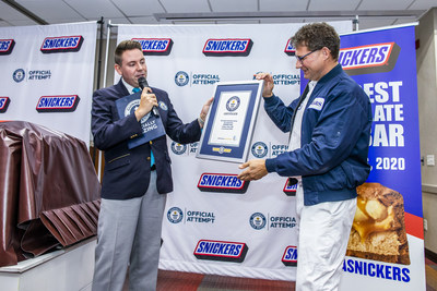 Guinness World Record adjudicator Michael Empric presents a title certificate to Mars Wrigley representative Ruud Engbers for the largest chocolate nut bar ever created Thursday, Jan. 16, 2020, in Waco, Texas. The more than two tons SNICKERS bar was made using a 1200 pound combination of caramel, nougat and peanuts, and 3500 pounds of chocolate.  (Drew Anthony Smith/AP Images for SNICKERS)