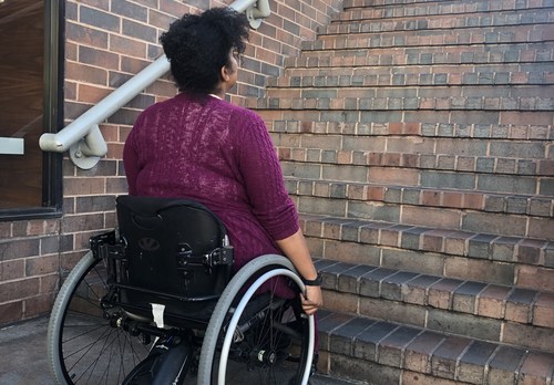 A young African American woman in a wheelchair looking up a flight of stairs