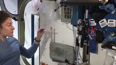 NASA astronaut Jessica Meir demonstrates how the LEctenna™, a light-emitting rectifying antenna constructed by the U.S. Naval Research Laboratory, converts electromagnetic waves into electric current on the International Space Station. Similar technology could be used on the Earth’s surface to convert electromagnetic waves beamed from space-based solar arrays. Photo courtesy of NASA.