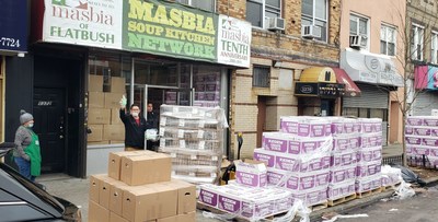 Masbia's Chef Ruben Diaz waving hand sanitizer and masks in front of Masbia of Flatbush with large pallets of Emergency Food such as kosher bread, chicken, vegetables, and juice are arriving to feed the needy.