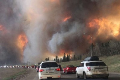 Residents evacuating while wildfire advances along evacuation route.