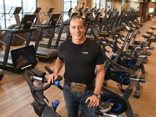 Life Time Founder, Chairman and CEO stands by a stationary bike inside a Life Time athletic resort.