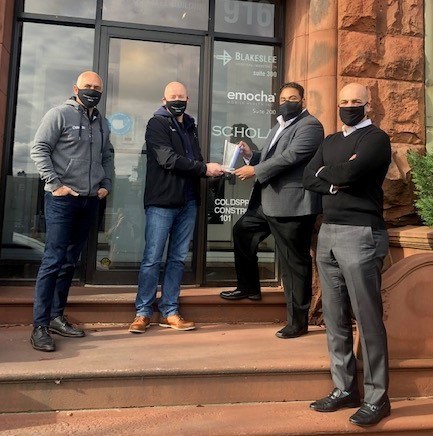 L-R Marc Bandini, Ostendio President and COO and Grant Elliott, Ostendio CEO and chairman present award to Ramon Castro, emocha CTO and Sebastian Seigeur, emocha CEO outside the emocha offices in Baltimore, MD.