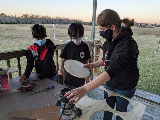 Amy Campbell (Systems Integration Co-Lead, Base Lead, CAD Specialist) demonstrates wheel routing with Jeremiah George and Albert Lee.