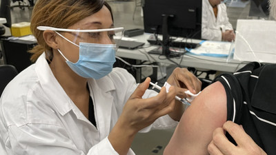 Health professional in goggles and mask administering COVID vaccine with needle in the shoulder of a sitting man. (CNW Group/Unifor)