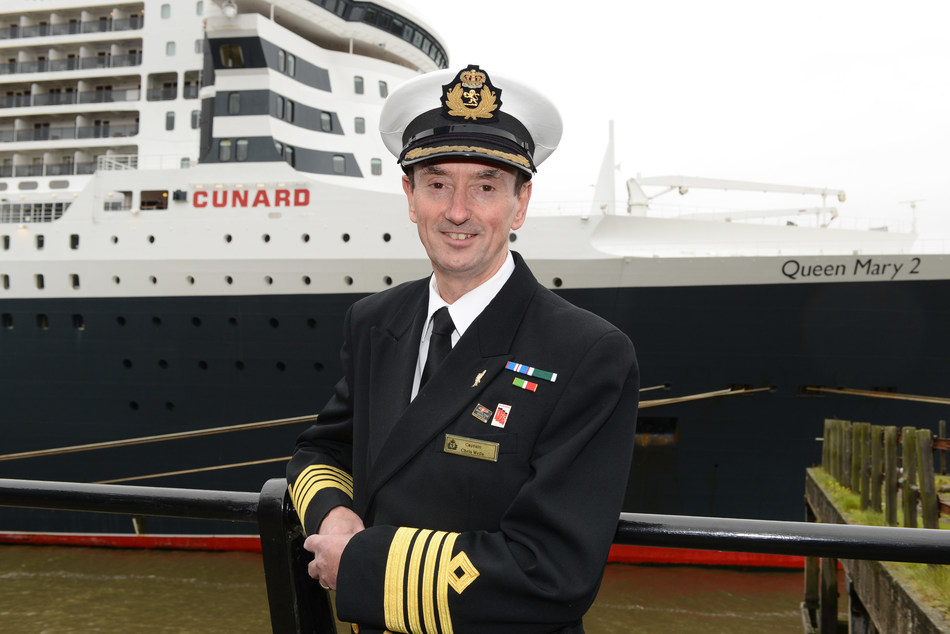 Cunard Captain Christopher Wells standing in front of flagship Queen Mary 2. As Wells embarked on his retirement this week, he was awarded the rank of Commodore in recognition of his 20 year career with the brand (April 2021)