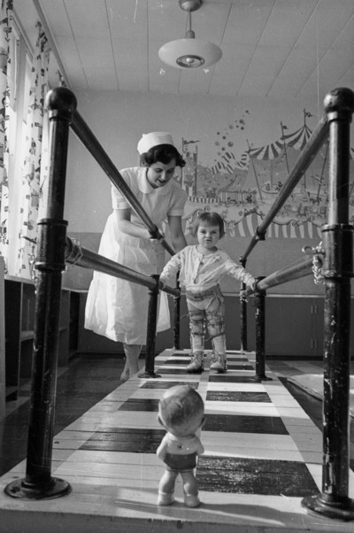 Mrs. E. Marr, physiotherapist, with Gifford, 2 1/2 yrs old, at the walking bars in the polio clinic at the Sudbury General Hospital, courtesy of Library and Archives Canada (CNW Group/Public Health Agency of Canada)