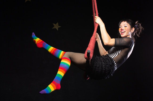 Rainbow-striped knee socks are modeled by a trapeze performer for sock retailer Cute But Crazy, online at https://crazysocks.com.