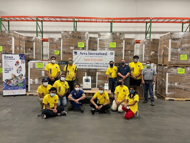 Sewa International Volunteers Gathered in the Sewa Warehouse in Atlanta, GA: Oxygen Concentrators Ready to be Shipped to India are seen in the Background.