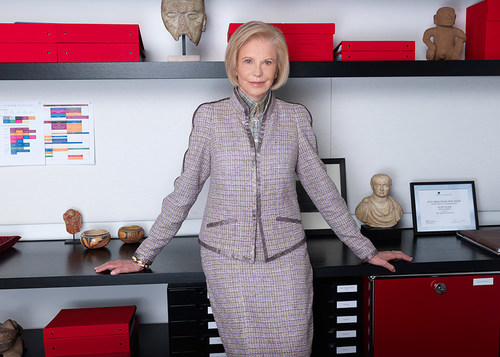 A photograph of Marica Vilcek in her office. Marica has chin-length blonde hair and wears a lavender suit.