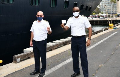 From Left to right, Koningsdam Captain Henk Draper and ship Hotel Director Errol Nelson, hold their COVID vaccine cards in front of Holland America Line's Koningsdam at the San Diego Cruise Terminal. Sharp HealthCare administered COVID vaccinations to the ship’s more than 100 crewmembers Wednesday morning.