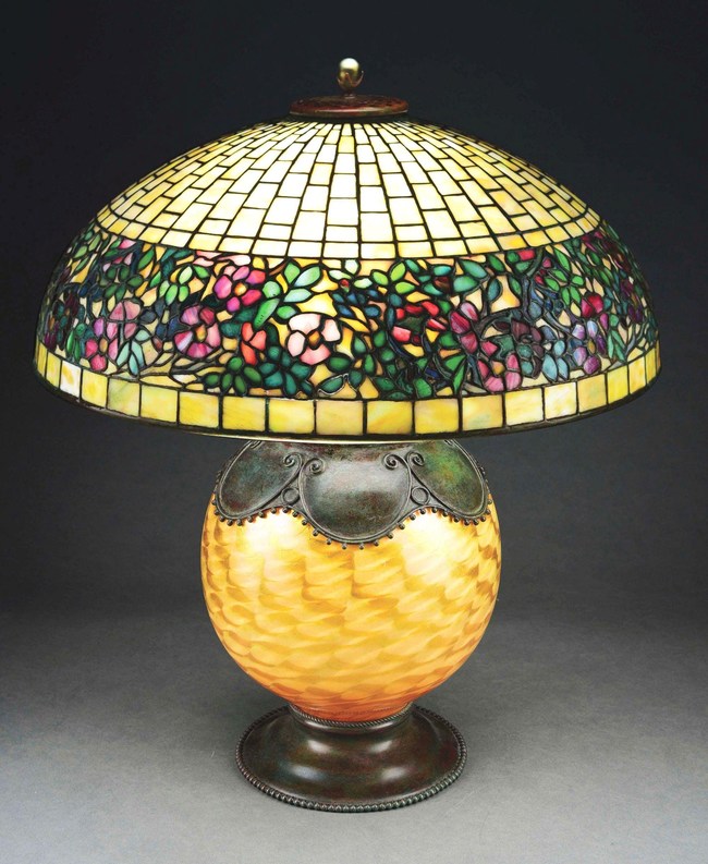 Tiffany Studios stained-glass Belted Rose table lamp, the shade displaying a belt of multicolored pink, red and white flowers; patinated bronze and yellow damascene Favrile decorated base. Double signed. Estimate $80,000-$100,000