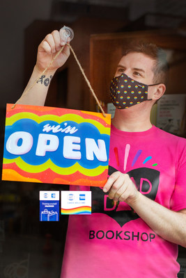 As stores gradually begin to reopen across the province of Ontario, small business manager M.J. Lyons from Glad Day Bookshop displays a “WE’RE OPEN” sign designed by Toronto artist, Amika Cooper on behalf of American Express Canada, to help welcome people back to Shop Small. Toronto ON. Photo Issue date: June 11, 2021. Photo Credit: Elaine Fancy (CNW Group/American Express Canada)