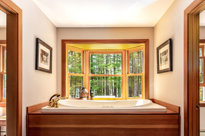 One of the main residence’s many oversized windows is shown here in the master bath, surrounding the spa tub. These windows allow ample natural light to fill the interiors, accenting its natural wood finishes while providing serene views of the great outdoors. LakefrontLuxuryAuction.com.