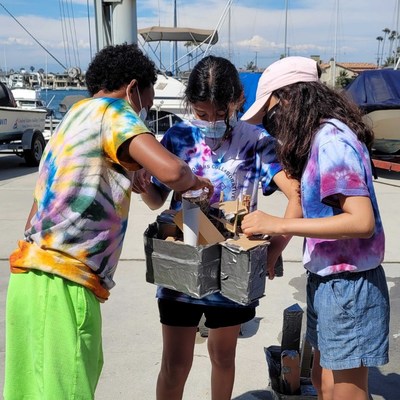 Long Beach, CA gifted middle school make last modifications before testing their floating city design at the US Sailing Center as part of the Dramatic Results summer STEAM camp.