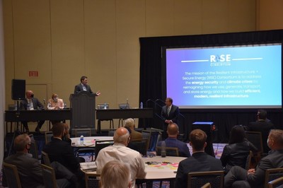 Michael Wu, Executive Director of the RISE Consortium (L, at podium), introduces Chris Van Metre (R, in front of screen), President & CEO of Advanced Technology International, during the RISE Consortium Member Meeting, Oct. 19 at the Gaylord National Resort & Convention Center in National Harbor, Md.