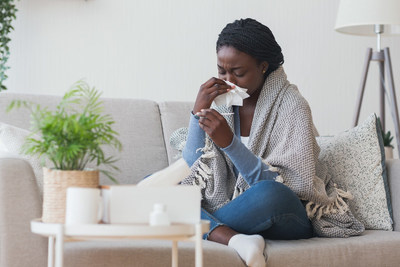 Woman on couch wiping nose with tissue and looking at thermometer. (CNW Group/Unifor)