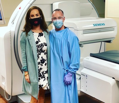 Founder + CEO of Accel Unite, Megan Eddings and Rolando Leal, healthcare hero, standing in front of a Siemens Healthineers Symbia Intevotm Excel. Rolando Leal, nuclear medicine technologist, loves the comfort and coolness of the Accel Unite Reusable Isolation gown.