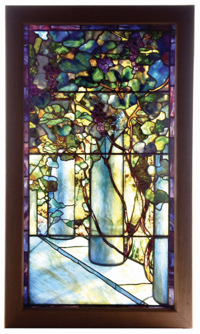 Spectacular Tiffany Studios leaded-glass window showing three columns with ascendant grapevines. Includes many examples of Tiffany's finest Favrile glass, including abundant confetti glass, streamers, ripple glass, mottles, and streaks. 55in x 32½ in by 6½ in. Estimate $70,000-$100,000