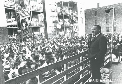 Dr. Martin Luther King Jr. addresses residents in an alley behind an apartment building on Chicago's West Side. King came o Chicago in 1966 to challenge slum conditions and racist policies. This historic moment was captured by legendary photographer John Tweedle, the first African American photographer to be hired by a major metropolitan daily newspaper. This and other rare photos of King taken by Tweedle are being offered as NFTs by the Obsidian Collection to be sold in the NFT marketplace