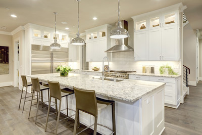 The white kitchen design features a large bar-style kitchen island with a granite counter top illuminated by modern pendant lights.  Stainless steel appliances framed by white shaker cabinets.  Northwest, United States