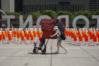 A mother and young child walk past 79 child mannequins on display at Nathan Phillips Square by the nonprofit World Vision Canada, each representing one million children who are trapped in child labour, Toronto, Saturday, June 11, 2022. The event, called #ChildLabour3D Experience, was organized ahead of World Day Against Child Labour, to engage Canadians to stand up for those 79 million children. (CNW Group/World Vision Canada)