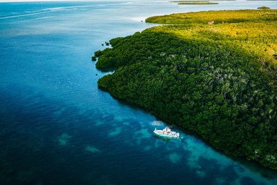 Drone photo of a boat near an island in beautiful colored water.