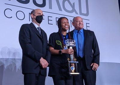 Genes in Space 2022 winner Pristine Onuoha accepts her trophy from miniPCR bio's Zeke Alvarez Saavedra (left) and Boeing's Scott Copeland (right). miniPCR bio and Boeing are the founding partners behind the Genes in Space competition.