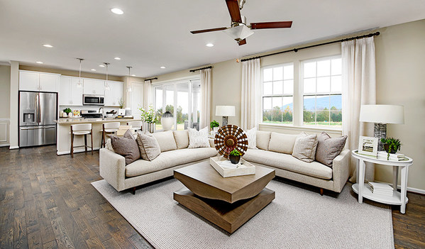 Living room with large couch, coffee table, and ceiling fan in front of kitchen with island