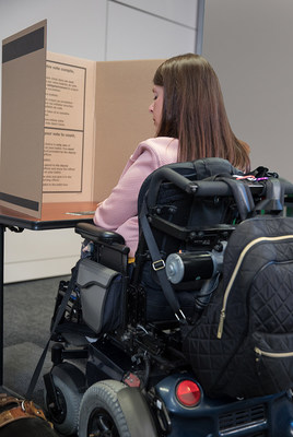 Électrice en fauteuil roulant avec son bulletin de vote dans un isoloir (Groupe CNW/Élections Québec)