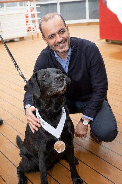 Gus Antorcha, Holland America Line President, poses with Joska, a 10-year-old black Labrador retriever, after she received her Platinum Medallion and 5-star Mariner Status for sailing 700 cruise days.