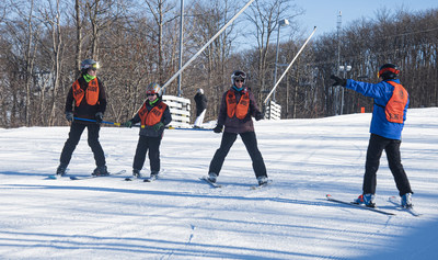 Two Sighted Guides flank a Blind Skier with an additional sighted observer on the right.