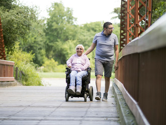 Women in a wheelchair with a caregiver walking in a park.