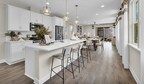 Bright kitchen with long island with three bar chairs and dining room behind it