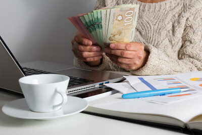 A person holding Canadian money sitting at a desk with bills and a laptop. (CNW Group/Unifor)