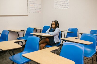 An Afro-Canadian/Black female student sits alone in an elementary school classroom, arms folded with a sad expression on her face. (CNW Group/Urban Rez Solutions)