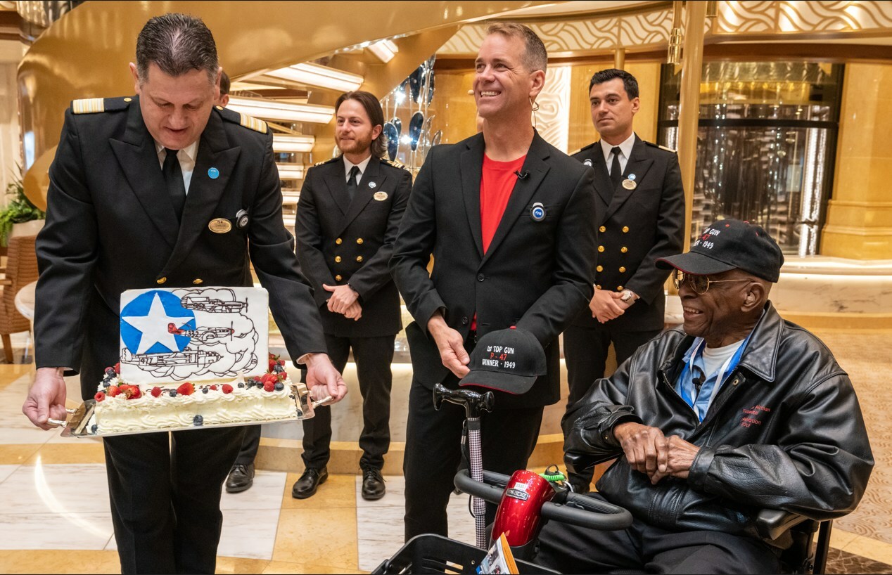 Princess Cruises President John Padgett, center, presents retired Lt. Colonel James H. Harvey III a cake on Discovery Princess to celebrate his 100th birthday (Image at LateCruiseNews.com - May 2023)