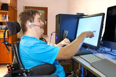 A person sitting in a wheelchair in front of a desk interacting with a computer monitor.