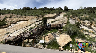 New stairway to viewing platform at "Crocodile Creek" on Dinosaur Ridge in Morrison, Colorado gives visitors a sense of the watery Cretaceous landscape now preserved in sandstone. A geometric Eolambia sculpture on the roadway depicts the type of dinosaurs that could've been crocodile prey at this site, long before the Rocky Mountains formed. Visitors can explore for free or pay for guided tours daily. Photo courtesy of Dinosaur Ridge.