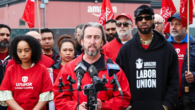 Gavin McGarrigle speaking in front of several microphones in front of a group of Unifor members wearing red shirts. (CNW Group/Unifor)