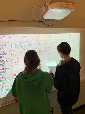 Two math students collaborate on a whiteboard.