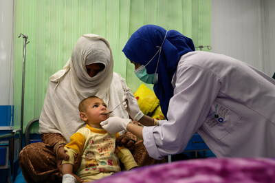 A nurse gives oral suspension to a 2-year-old boy suffering from malnutrition and pneumonia and sitting with his grandmother in an inpatient ward at Action Against Hunger’s therapeutic feeding unit in Kabul’s Ahmad Shah Baba Mina area on April 15, 2023. On the next bed is his 22-year-old mother sitting with his sick and severely malnourished 7-month-old brother who is also being treated at ACF’s TFU (Photo by Elise Blanchard for ACF).