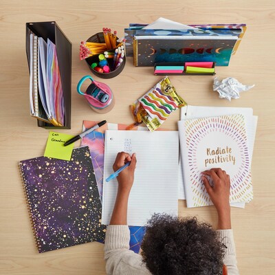 Top view of child surrounded by school supplies, writing in notebook.