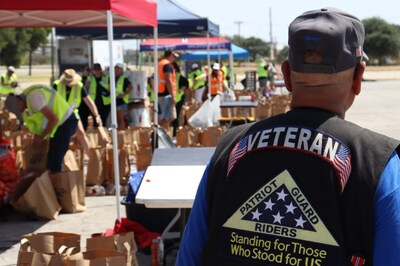 A Veteran watches as volunteers load bags of groceries at a food distribution event.