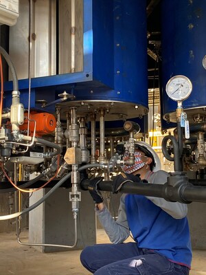 A worker installs an ultra-low-NOx hydrogen-powered industrial burner prototype for use in high-heat processes.