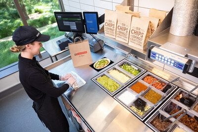 A Chipotle team member rolls a burrito while the automated makeline assembles a bowl.