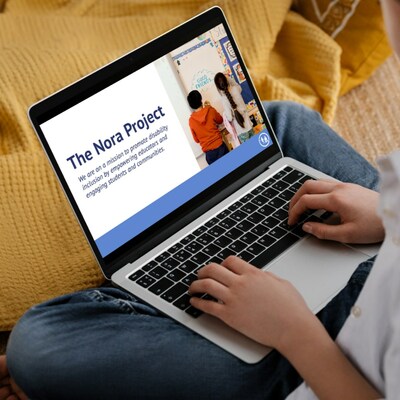 A person sits cross legged on a couch with a yellow blanket and a laptop on their lap. The laptop shows a presentation slide that reads 'The Nora Project: We are on a mission to promote disability inclusion by empowering educators and engaging students and communities.' To the right of the text is an image of two young students writing on a whiteboard.